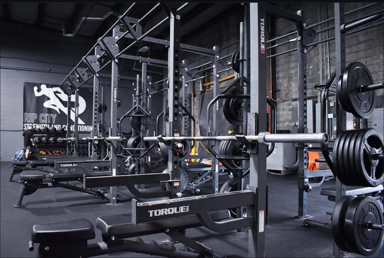 Rows of loaded squat racks and benches under the Rip City Strength and Conditioning banner
